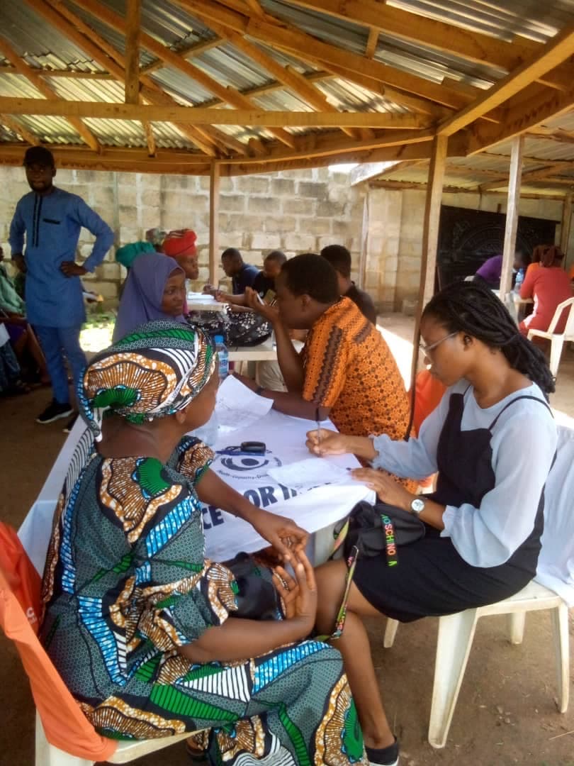 Women in traditional Yoruba dress receiving an intake consultation from a volunteer at a community outreach.