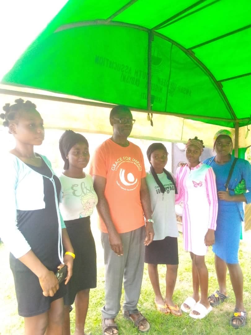 Five young women standing alongside a volunteer health worker under an open-air canopy at the outreach site.