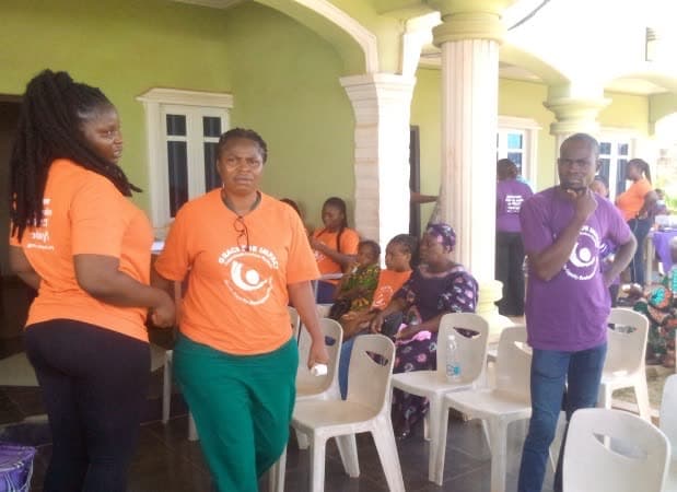 Volunteers in orange and purple shirts gathered with community members at the outreach venue.