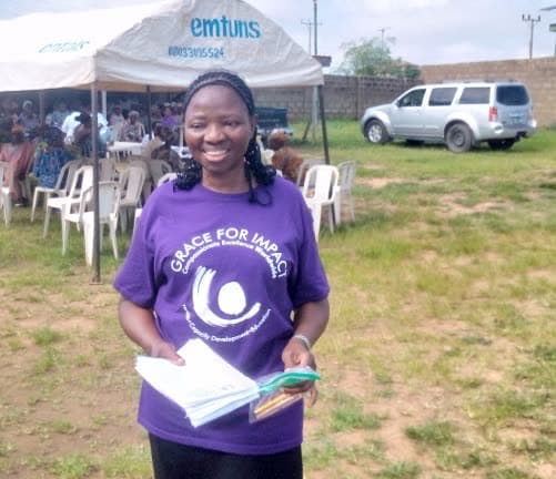A volunteer health worker holding documentation, smiling, at the outreach venue.